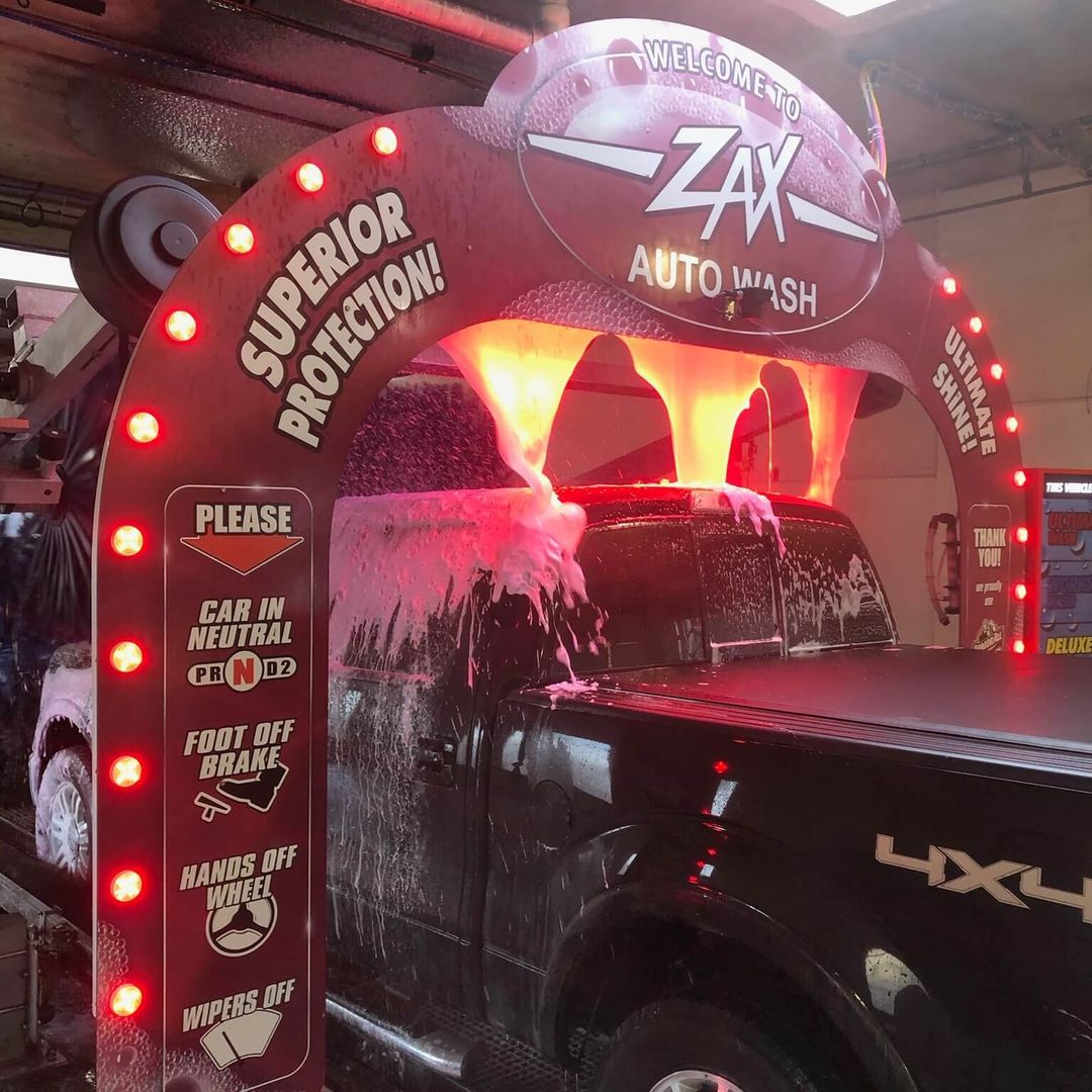 Zax auto wash tunnel opening with car driving through a wall of suds