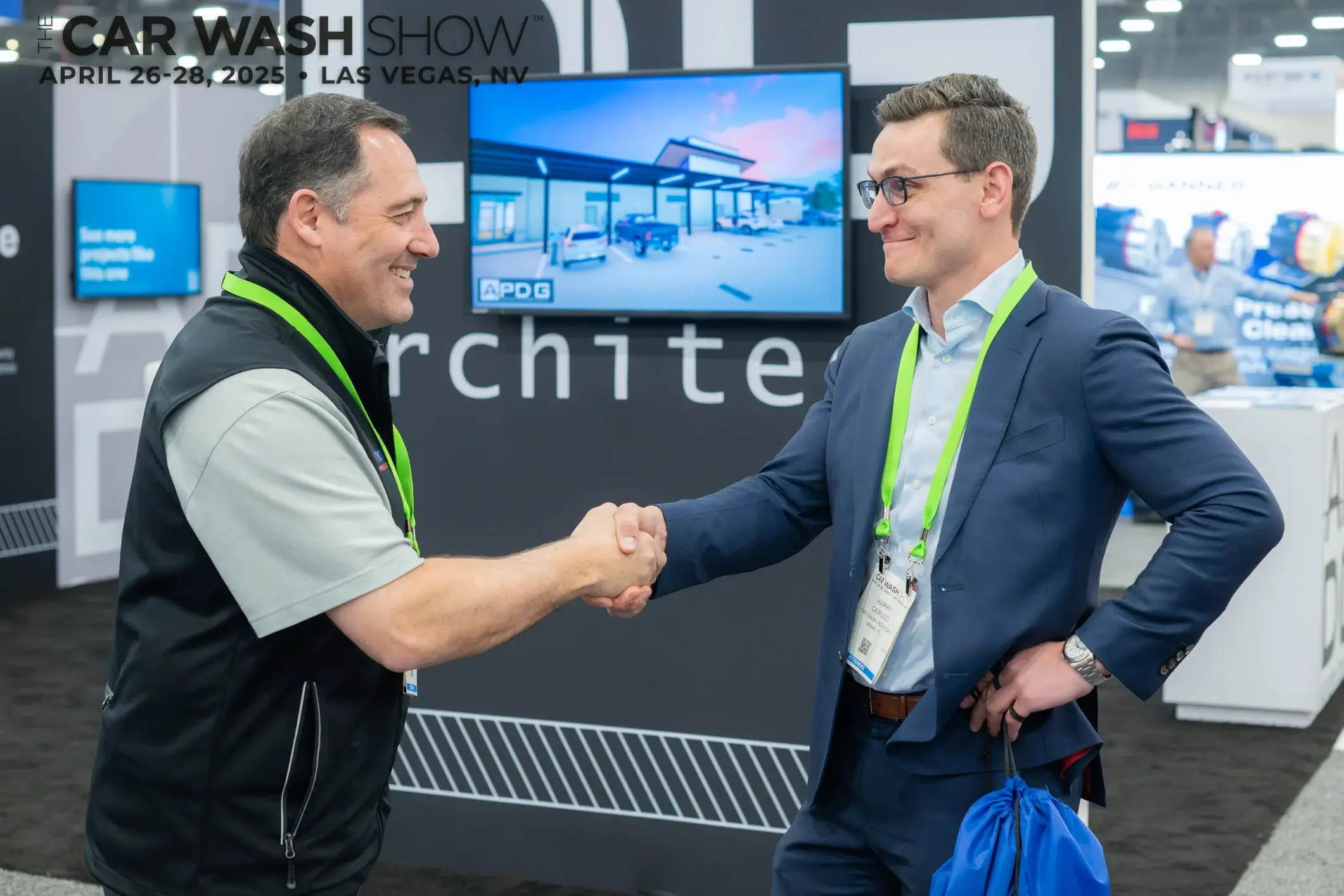 Two men in business attire shaking hands at a car wash industry trade show booth.